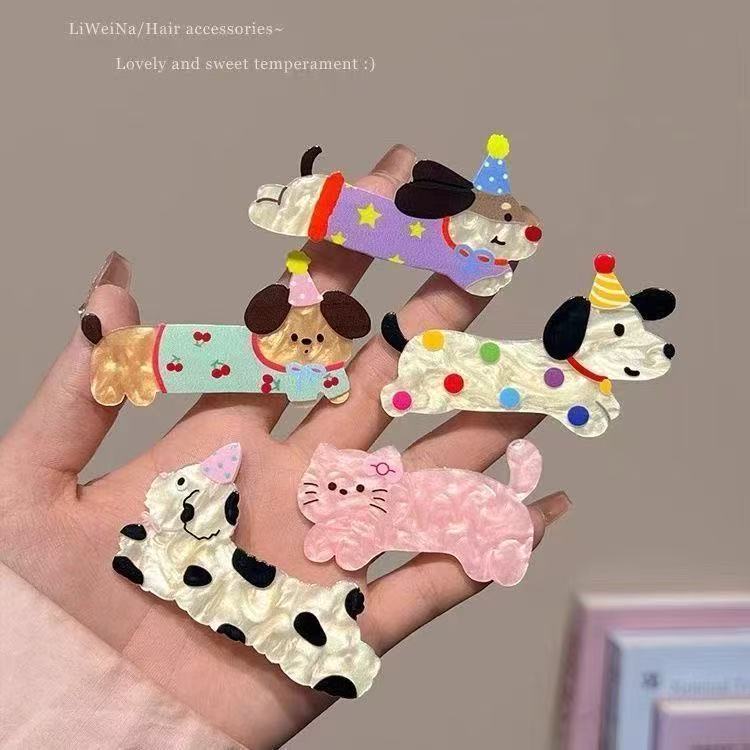 Hand holding five Party Animal acrylic hair clips including polka-dot dog, cherry pup, purple star dog, cow cat, and pink kitty